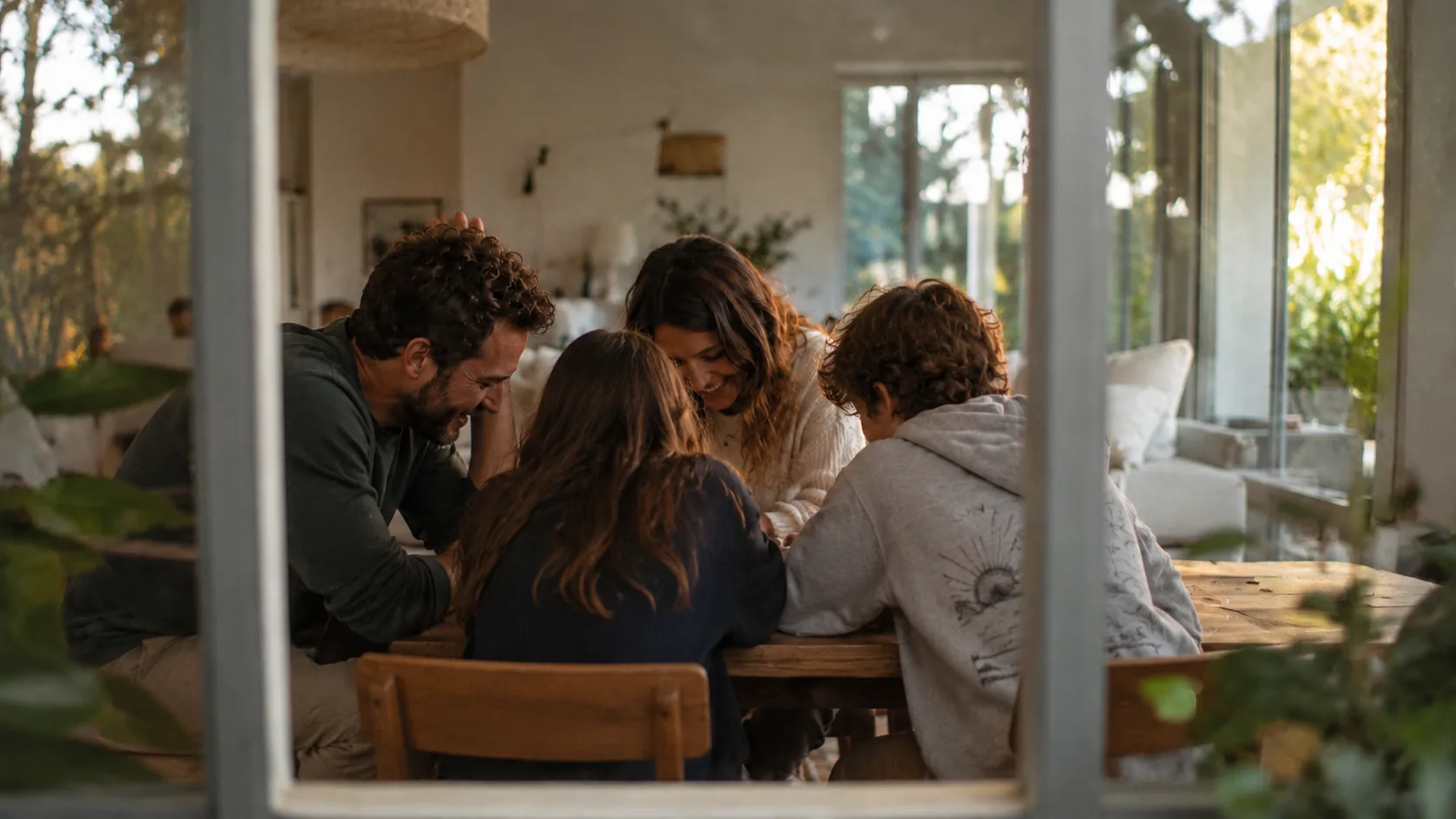 A family gathered close around a table together, seen through a window
